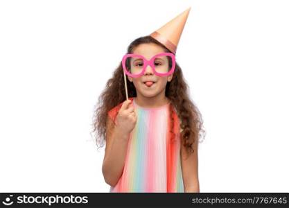 birthday, childhood and people concept - portrait of little girl in dress and party hat with glasses over white background. little girl in birthday party hat with glasses