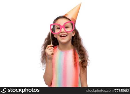 birthday, childhood and people concept - portrait of smiling little girl in dress and party hat with glasses over white background. little girl in birthday party hat with glasses