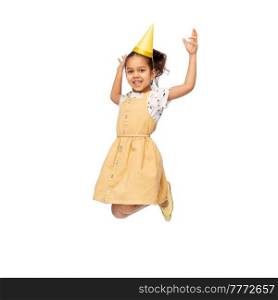 birthday, childhood and people concept - portrait of smiling little girl in dress and party hat jumping over white background. smiling little girl in birthday party hat jumping