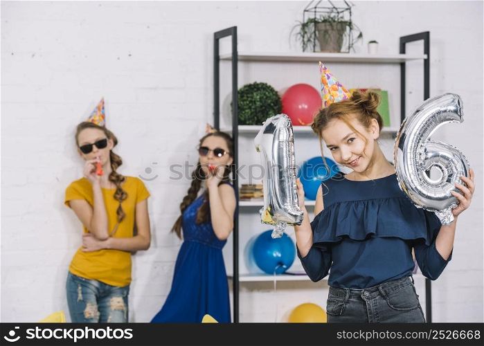 birthday girl showing numeral 16 foil silver balloons with her two friends blowing party blower