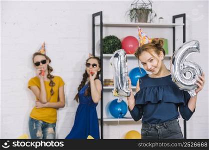 birthday girl showing numeral 16 foil silver balloons with her two friends blowing party blower