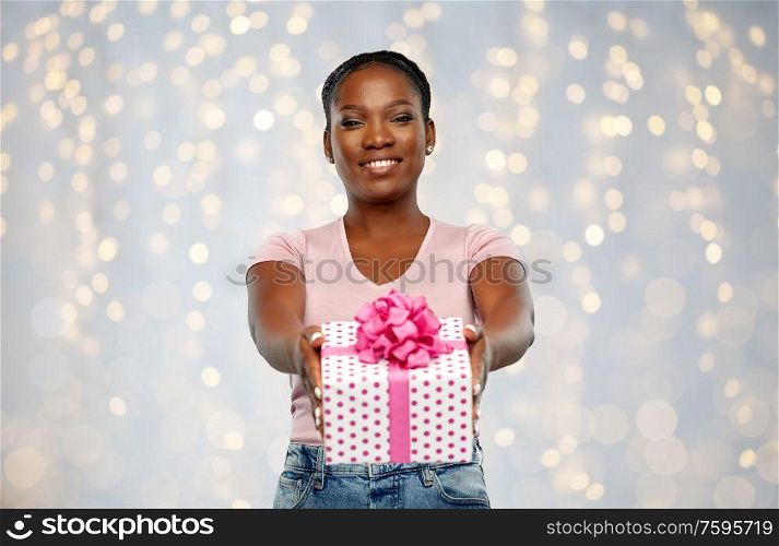 birthday, holiday and people concept - happy african american young woman with gift box over festive lights background. happy african american woman with birthday present