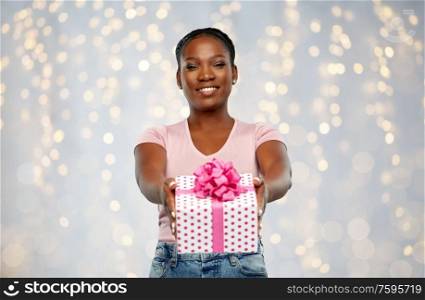 birthday, holiday and people concept - happy african american young woman with gift box over festive lights background. happy african american woman with birthday present