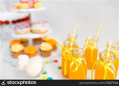 birthday party and drinks concept - orange juice in glass bottles with paper straws on table. orange juice in glass bottles with paper straws