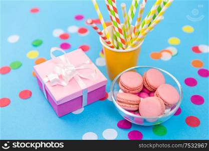 birthday party, celebration and decoration concept - gift box, pink macarons, paper straws and confetti on blue background. birthday gift, macarons and paper straws for party