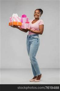 birthday present and surprise concept - happy african american young woman with gift boxes over grey background. happy african american woman with gift boxes