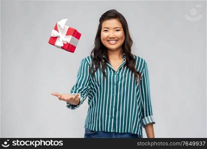 birthday present and surprise concept - happy asian young woman with gift box hanging in air over grey background. happy asian woman with birthday present