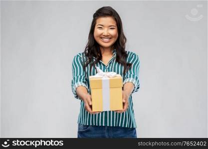 birthday present and surprise concept - happy asian young woman with gift box over grey background. happy asian woman with birthday present