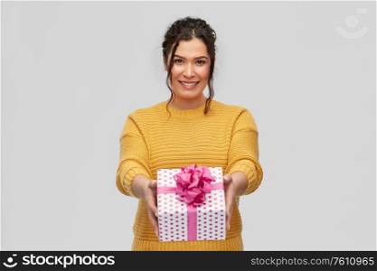 birthday present, surprise and people concept - portrait of happy smiling young woman with pierced nose holding gift box over grey background. smiling young woman holding gift box