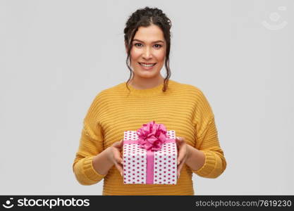 birthday present, surprise and people concept - portrait of happy smiling young woman with pierced nose holding gift box over grey background. smiling young woman holding gift box