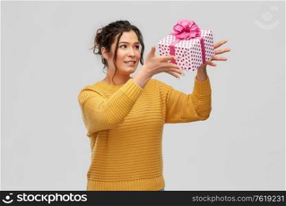 birthday present, surprise and people concept - portrait of happy smiling young woman with pierced nose throwing gift box over grey background. smiling young woman throwing gift box