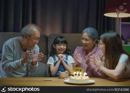Birthday surprise. Happy Asian family grandparents and mother celebrating enjoy birthday party with cake of granddaughter at home in night time