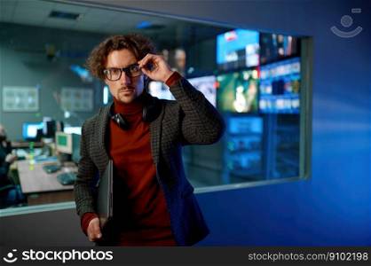 Bitcoin and crypto currency mining farm. Portrait of system administrator wearing eyeglasses, headphones and holding laptop standing in server datacenter hall. System administrator in eyeglasses in server datacenter hall