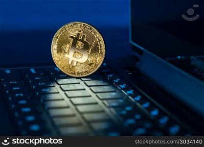 Bitcoin coin standing on keyboard of computer. Single bitcoin coin standing on the keyboard of modern laptop computer. Bitcoin coin standing on keyboard of computer