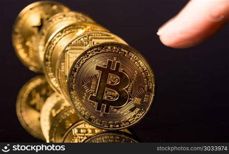 Bitcoins standing in a row like dominoes with finger. Bitcoin coins in a row on reflective surface with finger about to push them. Bitcoins standing in a row like dominoes with finger