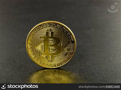 Bitcoins with black background with a single coin facing the camera in sharp focus with shading on the icon letter B on the face of the bit coin