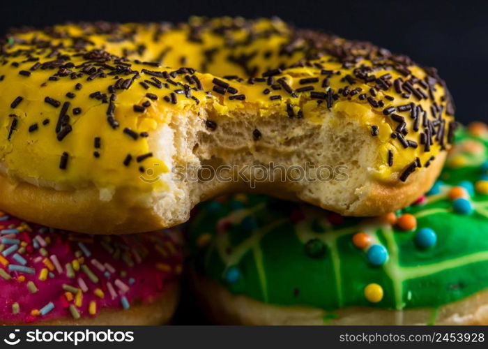 Bitten yellow glazed donut with sprinkles isolated. Close up of colorful donuts.