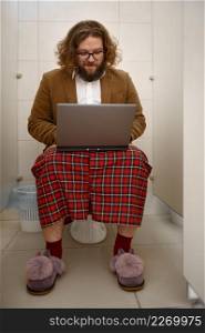 Bizarre businessman workaholic working online using laptop computer in lavatory. Telework. Freelance business man working laptop in lavatory
