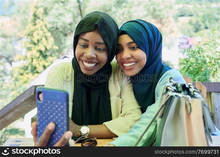 black african female friends using smart phone together wearing traditional islamic hijab clothes