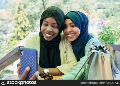 black african female friends using smart phone together wearing traditional islamic hijab clothes