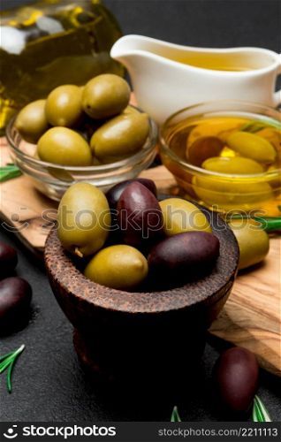 black and green olives and oil on wooden cutting board, dark concrete background. black and green olives and oil on wooden cutting board
