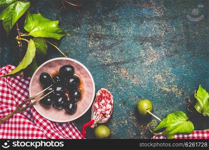Black and green olives on traditional red plaid napkin on dark rustic background, top view, place for text. Italian food background for menu or recipes .