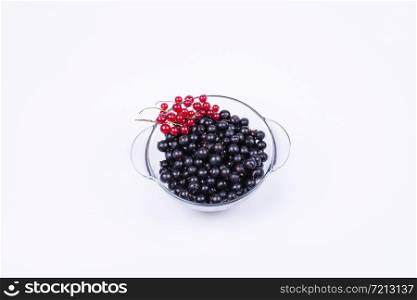 black and red currants in a transparent, glass bowl on a white background, top view. black and red currants