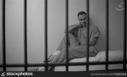Black and white A regretful inmate sitting on bed in prison
