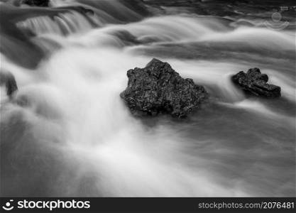 Black and white abstract of Rocks in stream with smooth flowing water with long exposure technique