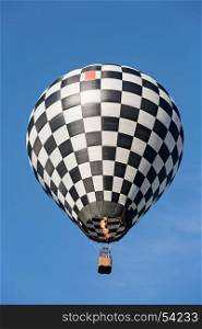 Black and white balloon in flight against a blue sky. Black and white balloon in flight