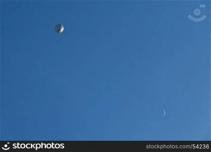 Black and white balloon in flight and moon seen from below against a blue sky. Black and white balloon in flight and moon seen from below