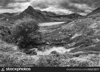 Black and white Beautiful panorama landscape image of stream flowing over rocks near Llyn Ogwen in Snowdonia during eary Autumn with Tryfan in background