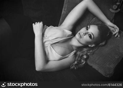 black and white beautiful woman , in fashion portrait , she is laying on a sofa i her living room , has blond long hair , and looking wth a dream expression