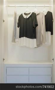 Black and white blouses hanging in white wardrobe