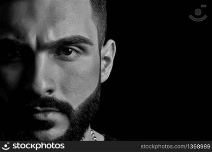 black-and-white close-up of a dramatic portrait of a young serious guy, a musician, singer, rapper with a beard in black clothes . half a face on a black isolated background.
