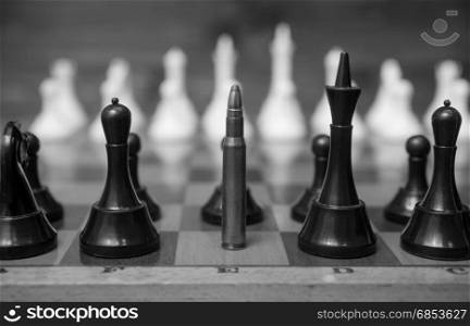 Black and white closeup photo of bullet in row of chess pieces. Conceptual photo of weapon power.