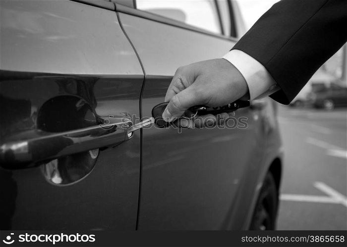 Black and white closeup photo of man inserting car key in the hole