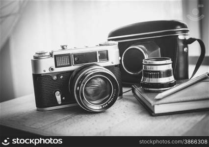 Black and white closeup photo of old camera and notebook lying on desk