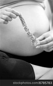 Black and white closeup photo of pregnant woman posing with measuring tape