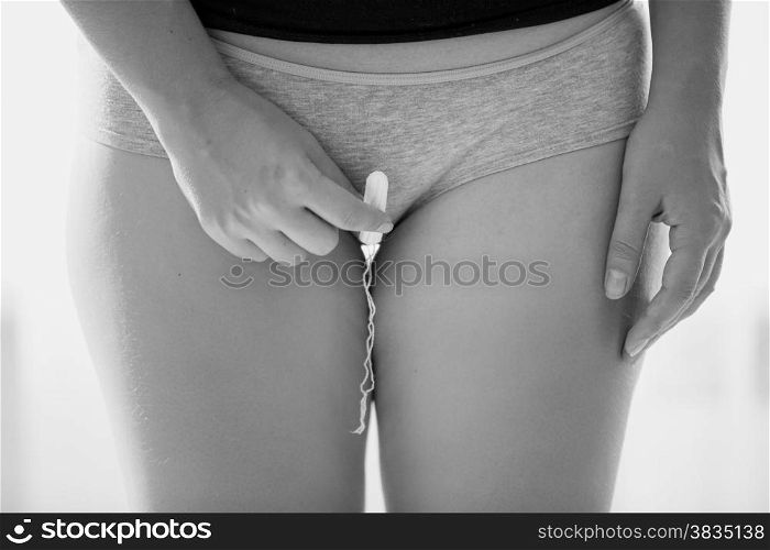 Black and white closeup photo of woman in panties holding menstrual tampon
