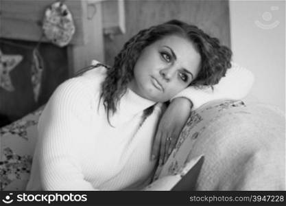 Black and white closeup portrait of cute woman in sweater sitting on sofa
