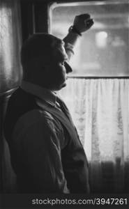 Black and white closeup portrait of handsome man in suit looking out of window in retro train