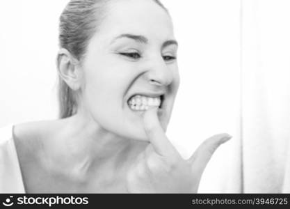 Black and white closeup portrait of young woman looking in mirror and checking teeth