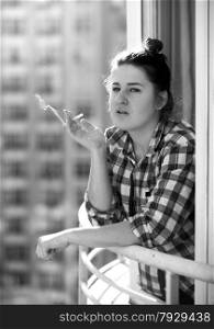 Black and white closeup portrait of young woman smoking on balcony