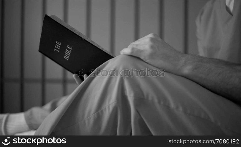 Black and white dolly shot of an inmate reading a bible in prison