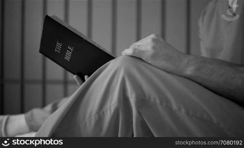 Black and white dolly shot of an inmate reading a bible in prison