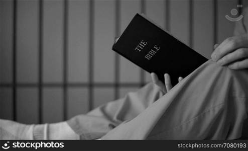 Black and white dolly shot of an inmate rstudying the bible in prison