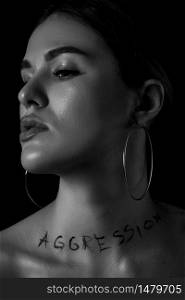 black and white dramatic portrait of a young woman with the inscription aggressive on a black background. the inscription is written in the photographer&rsquo;s hand using mascara ,not a tattoo.