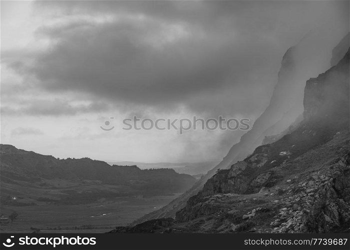 Black and white Epic mountain landscape image of Pen Yr Ole Wen in Snowdonia National Park with low cloud on peak and dramatic view