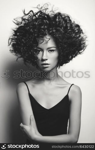 Black and white fashion studio portrait of beautiful woman in black dress with afro curls hairstyle. Fashion and beauty
